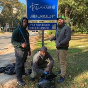 Three Tallahassee Little Guys Movers employees in front of Adopt a Street sign