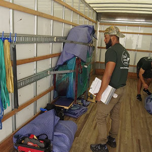 Little Guys Movers employees moving a grand piano in moving truck