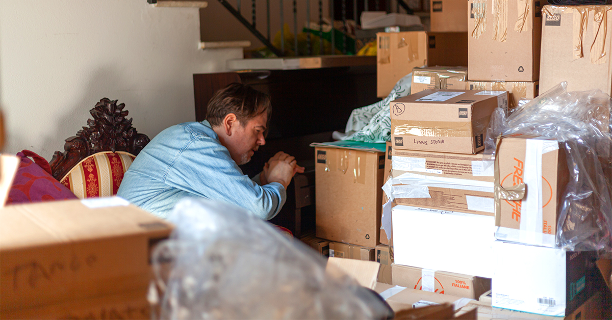 A person crouches down, looking carefully at a large stack of moving boxes.