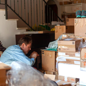 A person crouches down, looking carefully at a large stack of moving boxes.