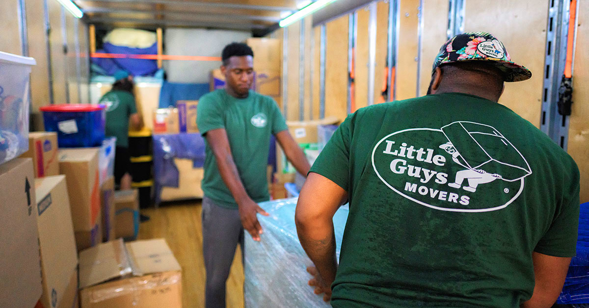 Two Little Guys Movers carefully move a piece of heavy furniture into the moving truck.