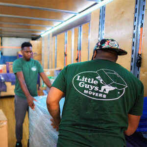 Two Little Guys Movers carefully move a piece of heavy furniture into the moving truck.